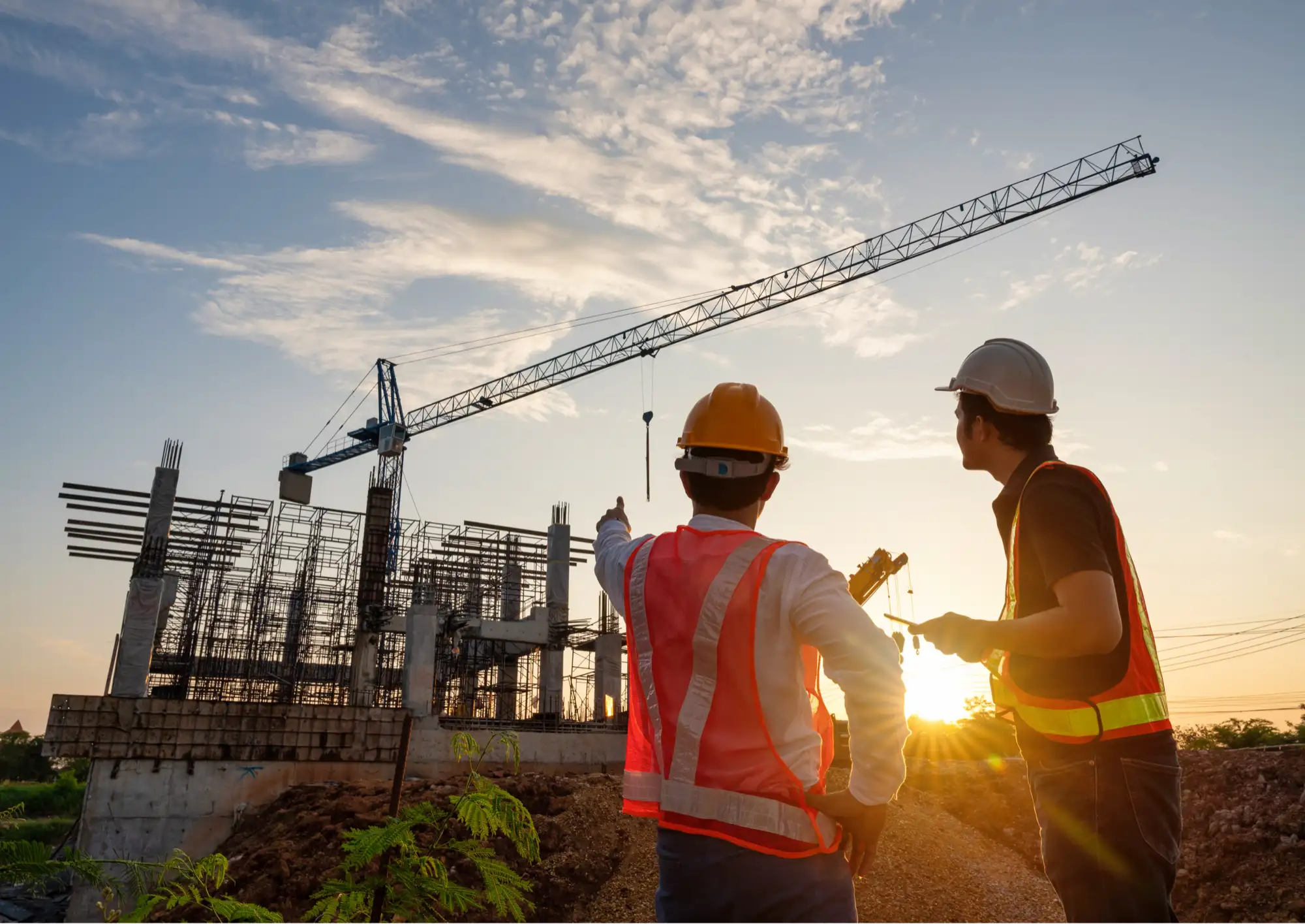 Construction team pointing toward a crane on site at sunset